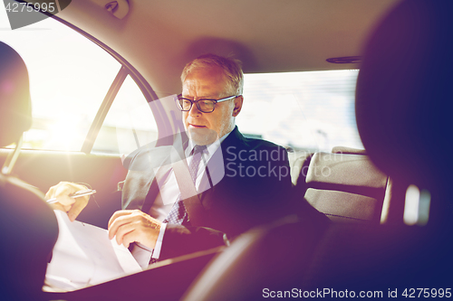 Image of senior businessman with papers driving in car