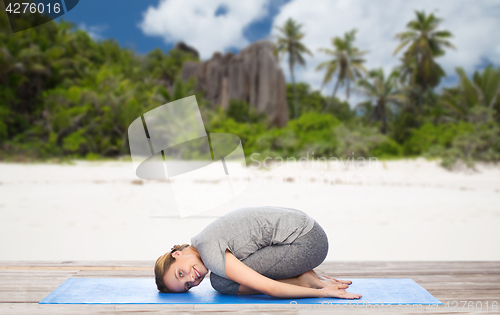 Image of happy woman doing yoga in child pose on beach