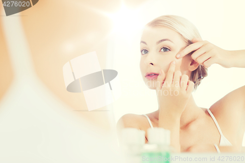 Image of woman squeezing pimple at bathroom mirror