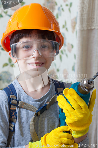 Image of boy in a construction helmet and safety goggles with a drill in 