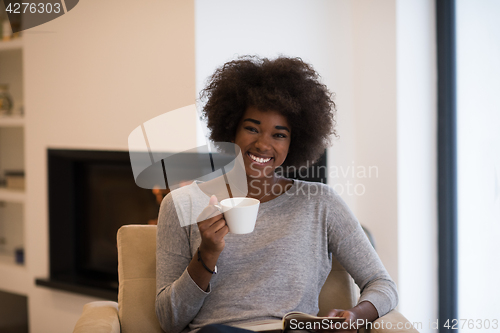 Image of black woman reading book  in front of fireplace