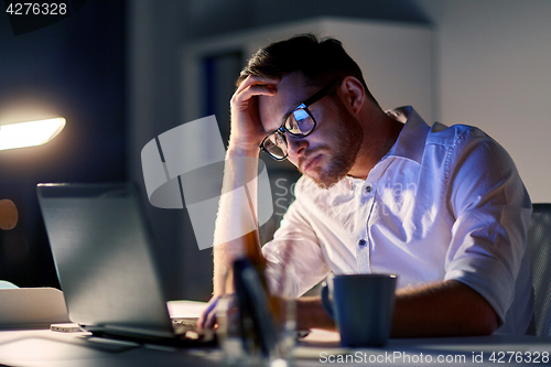 Image of businessman with laptop thinking at night office