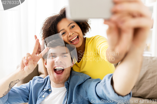 Image of happy couple with smartphone taking selfie at home