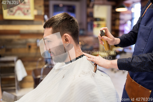 Image of barber applying styling spray to male hair at shop