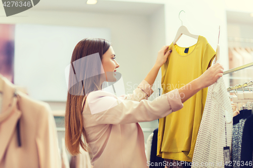 Image of happy young woman choosing clothes in mall