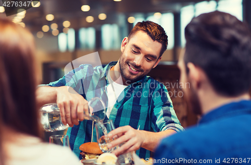 Image of happy man with friends pouring water at restaurant