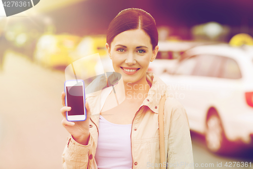 Image of smiling woman showing smartphone over taxi in city