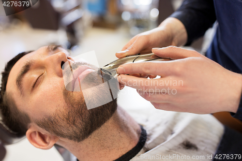 Image of man and barber with trimmer cutting beard at salon