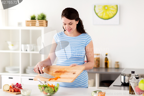 Image of pregnant woman cooking vegetable salad at home