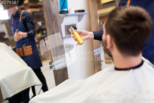 Image of barber showing hair styling spray to male customer