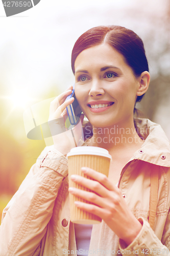 Image of smiling woman with smartphone and coffee in park