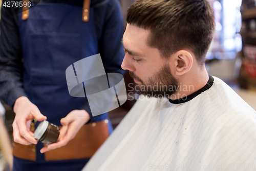 Image of barber showing hair styling wax to male customer