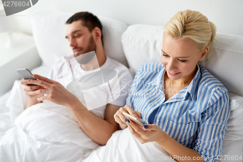 Image of couple with smartphones in bed at home