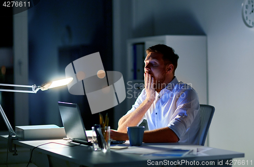 Image of man with laptop and coffee working at night office