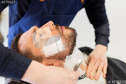 Image of man and barber with straight razor shaving beard