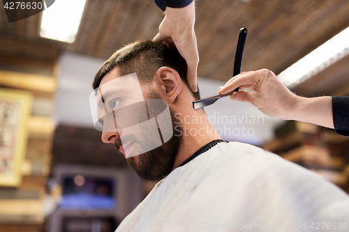 Image of man and barber with straight razor shaving hair