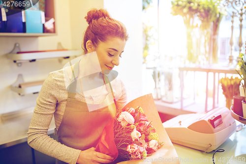 Image of smiling florist woman packing bunch at flower shop