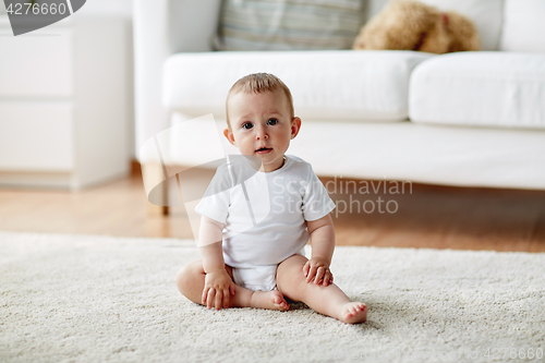 Image of happy baby boy or girl sitting on floor at home
