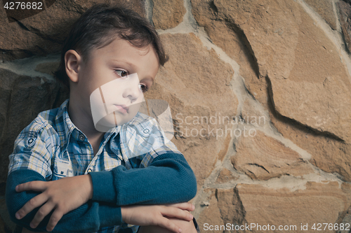 Image of sad little boy sitting near the wall