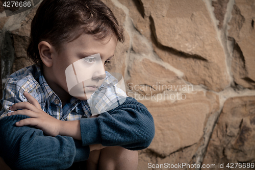 Image of sad little boy sitting near the wall