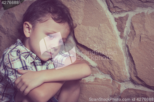 Image of sad little boy sitting near the wall