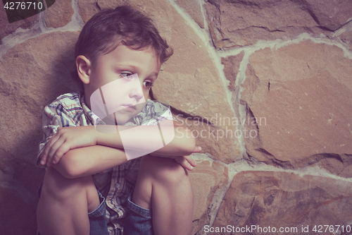 Image of sad little boy sitting near the wall