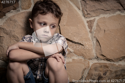 Image of sad little boy sitting near the wall