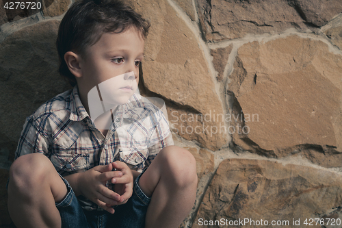 Image of sad little boy sitting near the wall