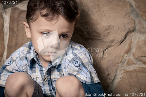 Image of sad little boy sitting near the wall