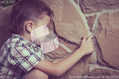 Image of sad little boy sitting near the wall