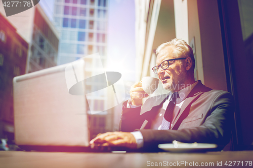 Image of senior businessman with laptop drinking coffee