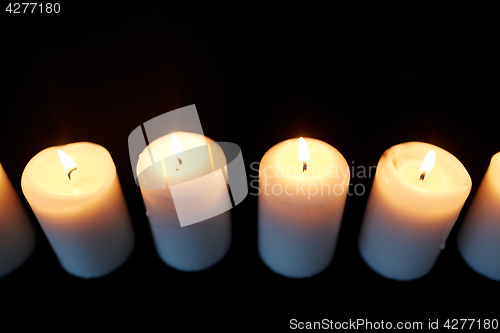 Image of candles burning in darkness over black background