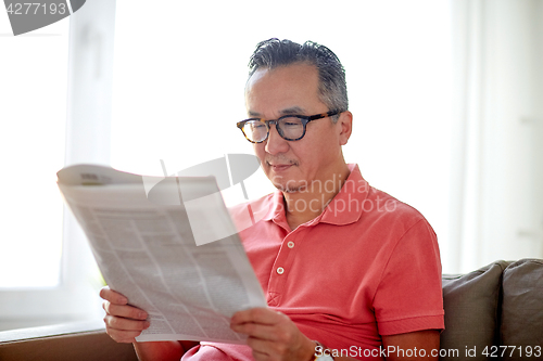 Image of happy man in glasses reading newspaper at home