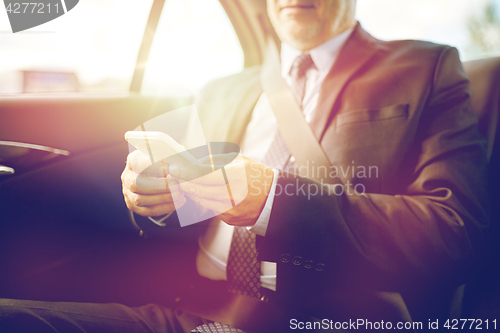 Image of senior businessman texting on smartphone in car