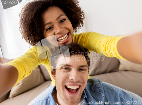 Image of happy multiethnic couple taking selfie at home