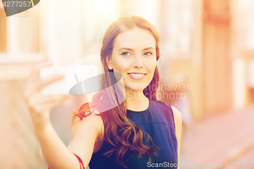 Image of happy woman taking selfie with smartphone in city