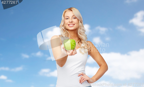 Image of happy young woman with green apple over blue sky