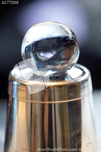 Image of hand-cut ice ball on top of cocktail shaker at bar