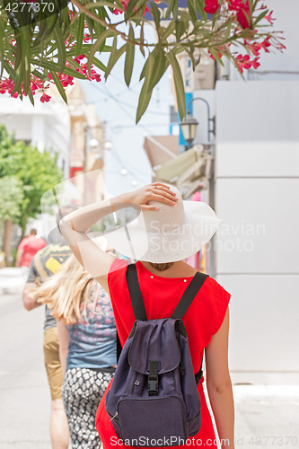 Image of Woman in red dress, white hat and backpack walking in town