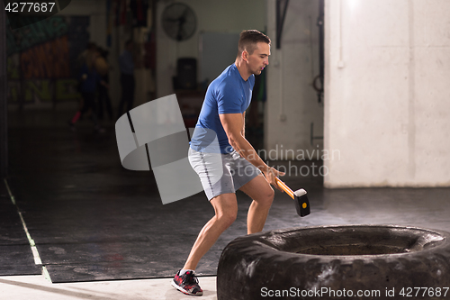 Image of man workout with hammer and tractor tire