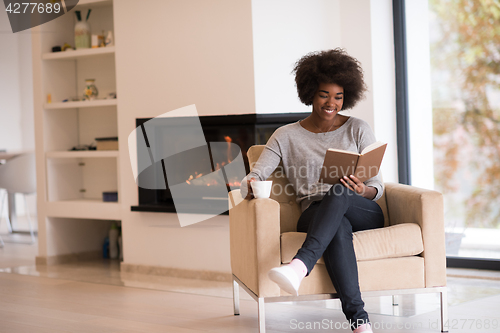 Image of black woman reading book  in front of fireplace