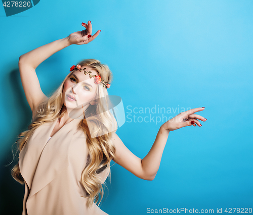 Image of young pretty blond girl with curly blond hair and little flowers happy smiling on blue sky background, lifestyle people concept 