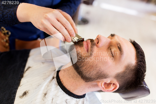 Image of man and barber with trimmer cutting beard at salon