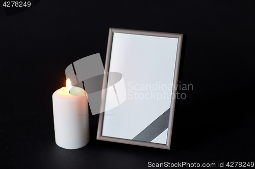 Image of black ribbon on photo frame and candle at funeral