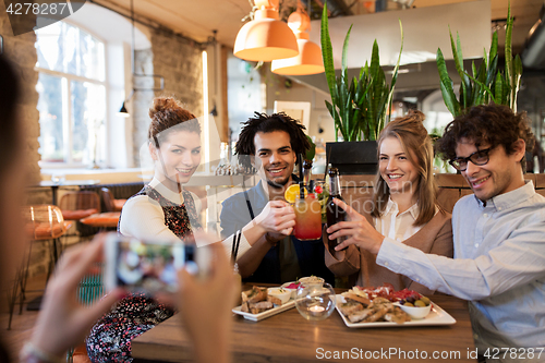 Image of happy friends clinking drinks at bar or cafe