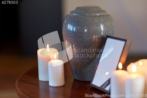 Image of photo frame, cremation urn and candles on table