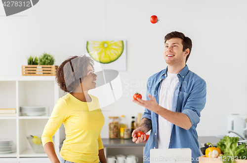 Image of couple cooking food and juggling tomatoes at home