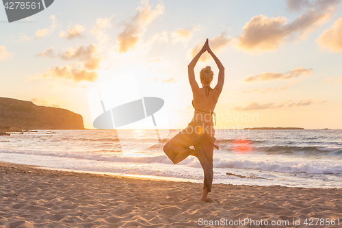 Image of Woman practicing yoga on sea beach at sunset.
