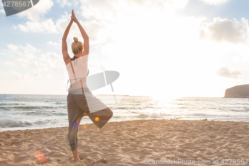 Image of Woman practicing yoga on sea beach at sunset.