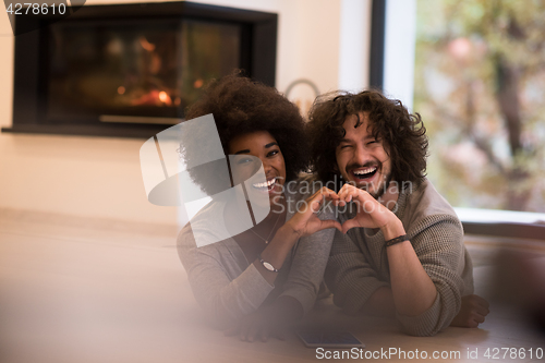 Image of multiethnic couple showing a heart with their hands on the floor